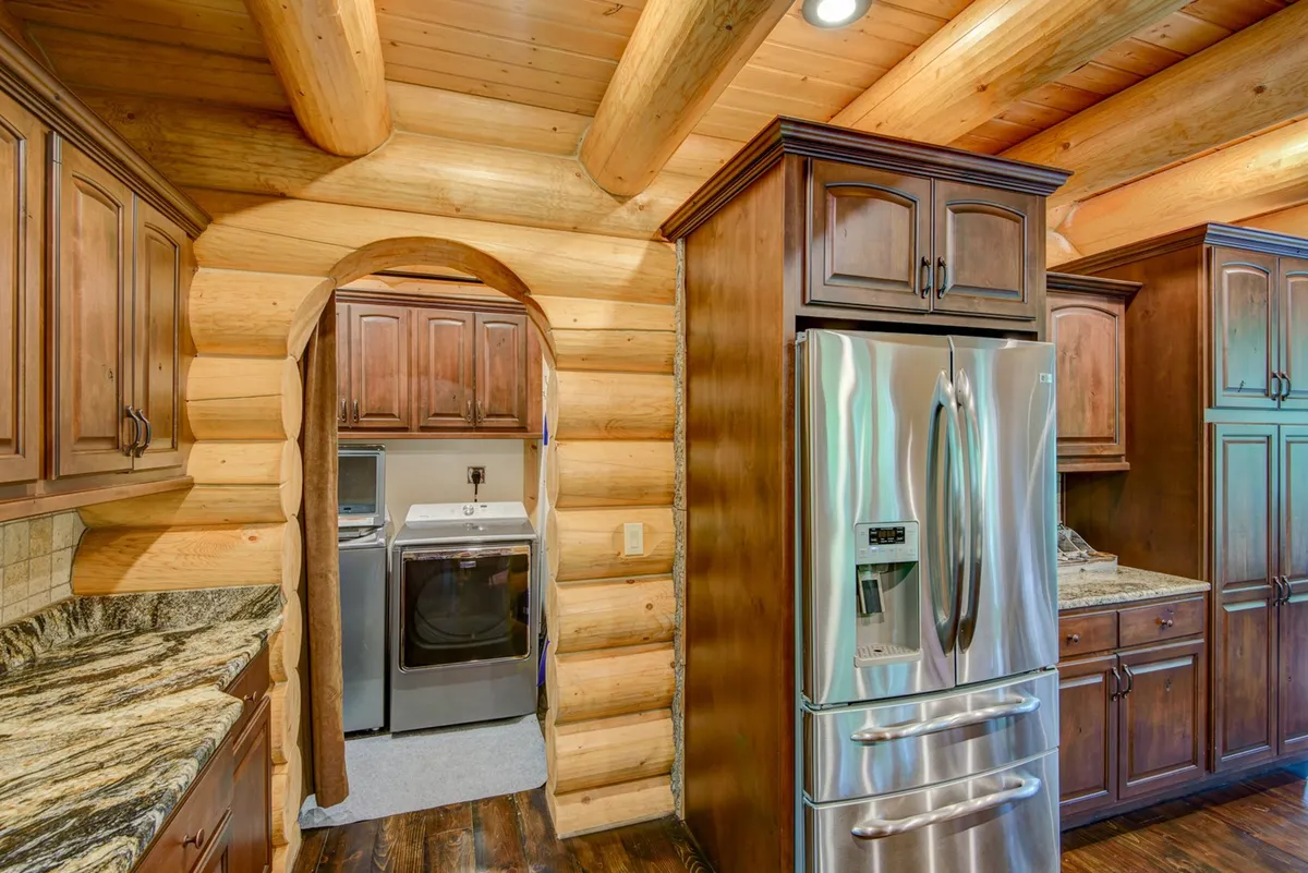 A kitchen with log walls, granite countertops, and stainless steel appliances. The layout supports meal prep, family gatherings, and includes elements that hint at the laundry area's proximity, such as practical counter space.