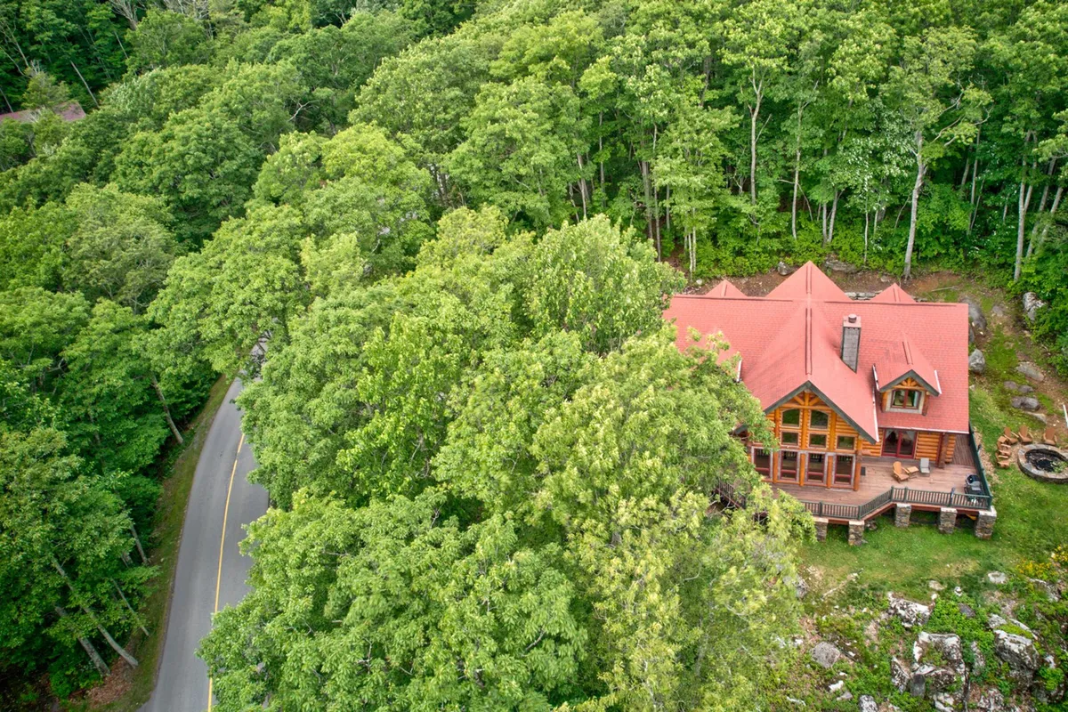A tranquil exterior shot showcasing a wooden cabin surrounded by greenery, a spacious deck area, and a fire pit ready for evening gatherings. The deck and fire pit area are designed for relaxation, group games, and enjoying the outdoors, with ample space for family activities.