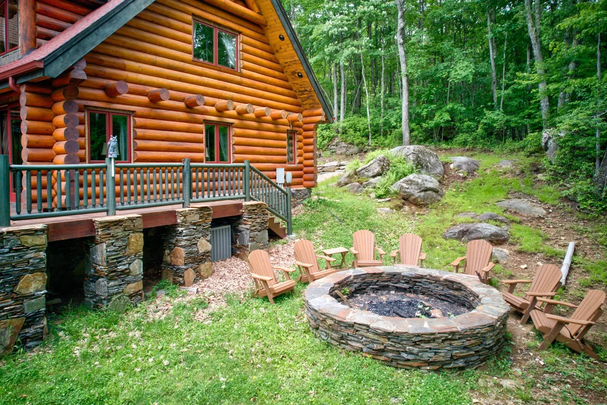 An inviting exterior scene with a log cabin, a blazing fire pit surrounded by comfortable outdoor seating, and families gathered to enjoy the evening. The area is set amidst natural greenery, emphasizing communal moments, outdoor dining, and the classic campfire experience under the stars.
