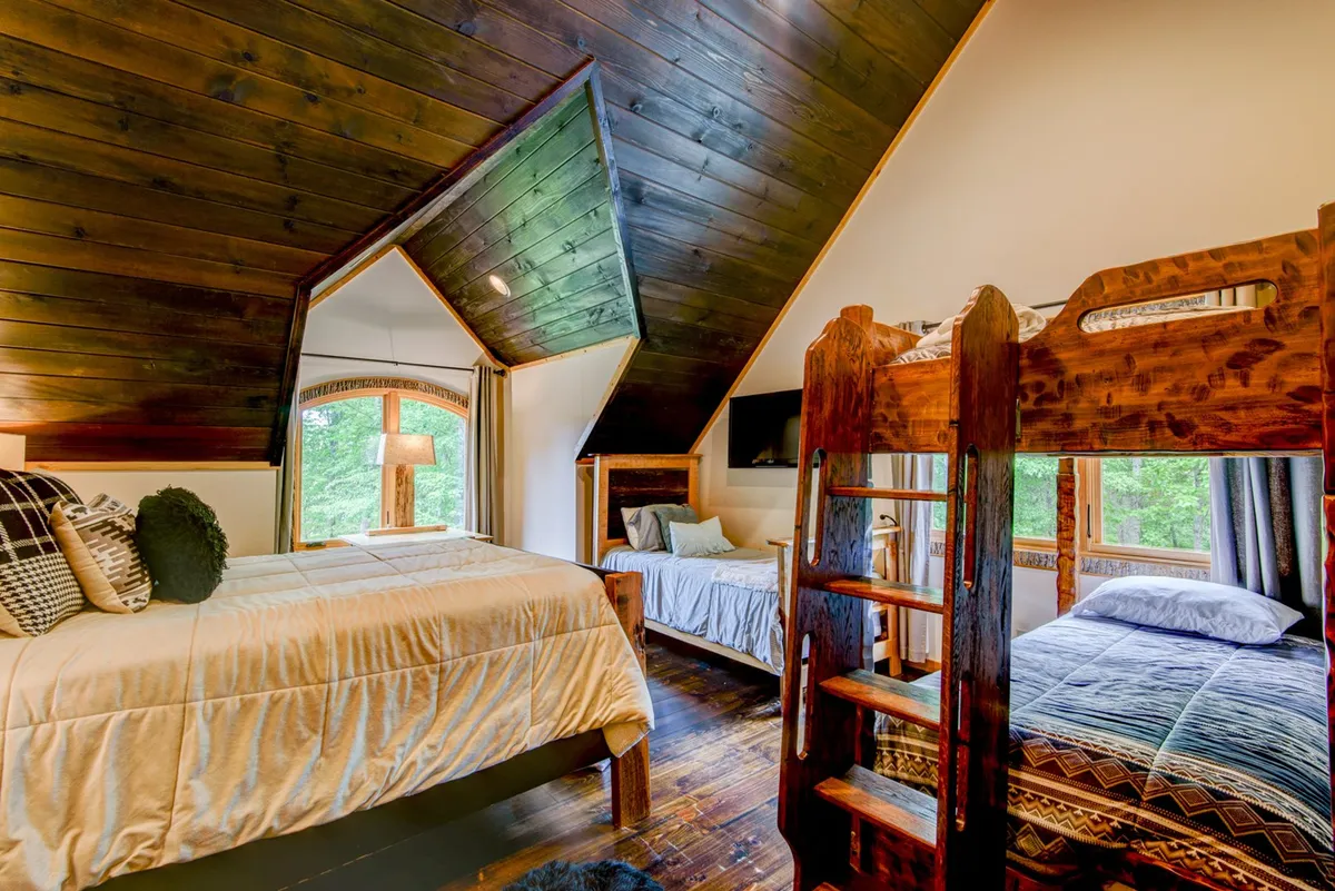A warm and welcoming upstairs bedroom with exposed wooden beams, a bunk bed, and a large window streaming in natural light. Textured bedding adds comfort, and the space feels perfect for families or children, with room for reading or evening storytelling by the window.