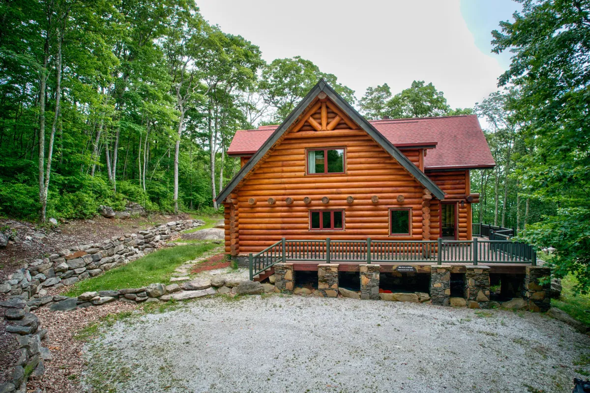 This image features the lodge’s log cabin structure with large windows and a welcoming deck area. The space is set up for gatherings or casual outdoor barbecues, with visible seating and greenery, inviting guests to socialize and enjoy fresh air. Its warm lighting suggests an inviting space for evening relaxation.