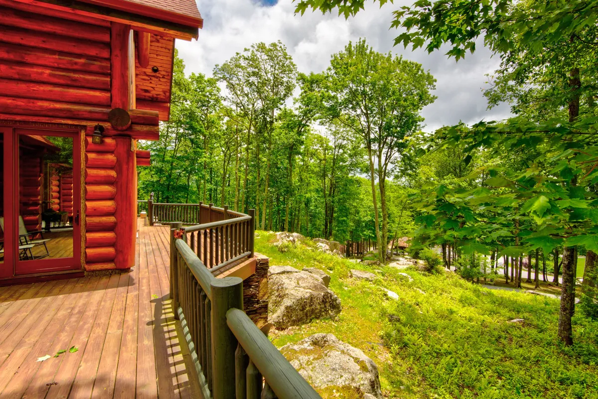 The image showcases the lodge’s log cabin structure nestled amid lush greenery and rock formations, with a broad wooden deck overlooking the natural surroundings. The setting conveys peace and privacy, emphasizing the lodge’s connection to its environment and its suitability for alfresco dining or quiet moments outdoors.
